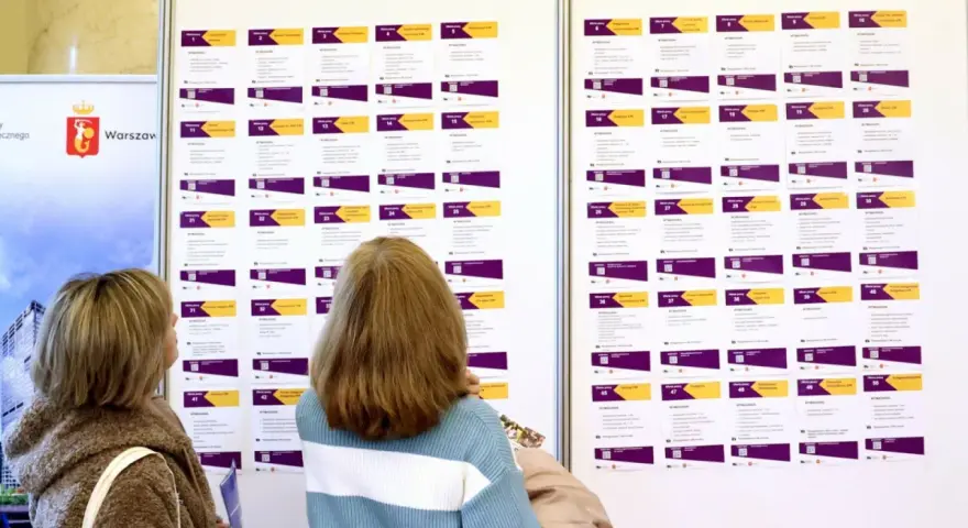 Dwie kobiety przeglądają tablicę z ofertami pracy, szukając rozwiązań problemu bezrobocia w Polsce.