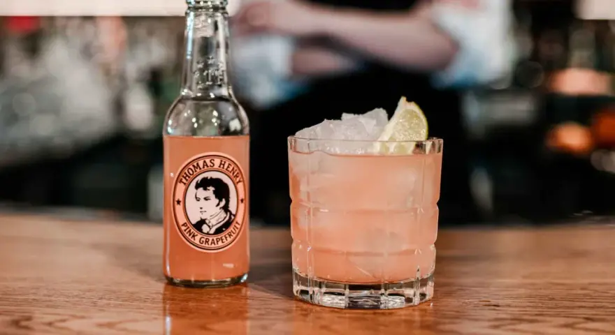 En rosa tequila drink med is och lime, bredvid en flaska Thomas Henry Pink Grapefruit.