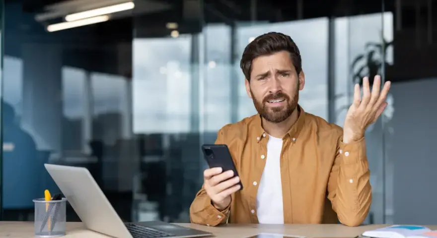 Zdezorientowany mężczyzna trzyma telefon, jakby właśnie dowiedział się o problemach z cesją.