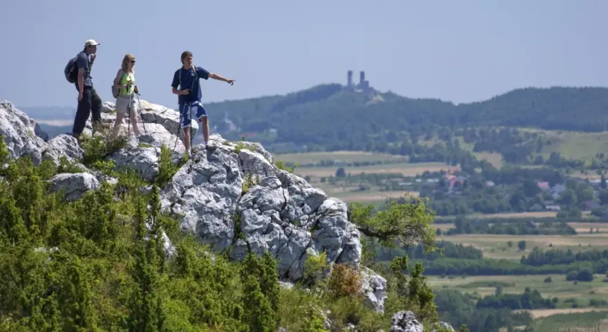 Trzech turystów na skalistym szczycie, wskazując na ruiny zamku w oddali. Piękne krajobrazy gór Kielc.