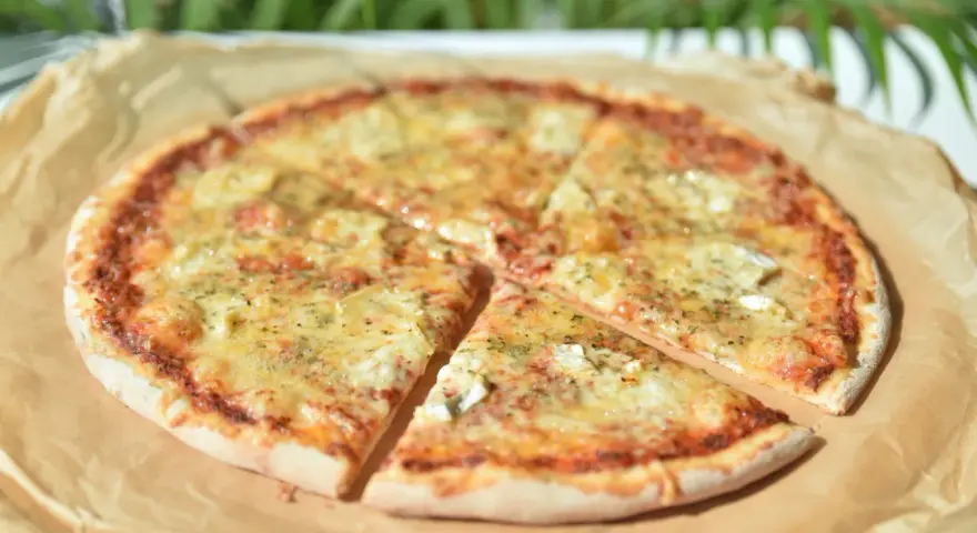 Pizza 4 sery z roztopionym serem i ziołami na papierze do pieczenia.