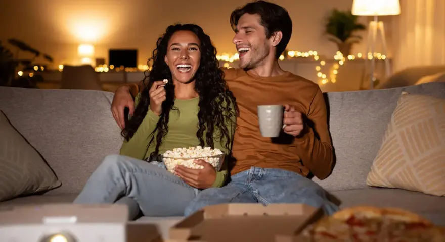 Ein lachendes Paar genießt einen gemütlichen Filmabend mit Popcorn und Pizza. Perfekte filmabend snacks für einen entspannten Abend.