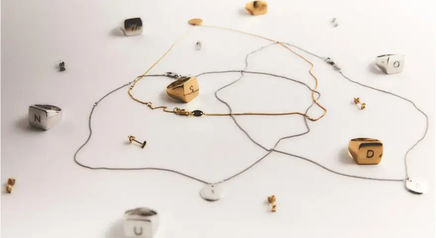 Joyas con letras, como limpiar la plata para que brillen. Anillos y collares dorados y plateados sobre fondo blanco.