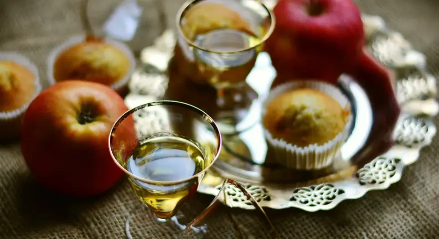 Zwei Gläser mit goldenem Schnaps, Äpfel und Muffins auf einem Silbertablett. Perfekt für den Genuss von selbstgemachtem Kartoffelschnaps.