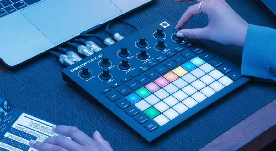 Ręce tworzą muzykę na Novation Circuit Rhythm, z podłączonym laptopem i kablami.