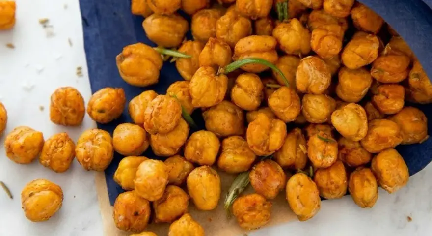 Un sacchetto blu rovesciato rivela una montagna di ceci croccanti al forno, dorati e invitanti, con qualche rametto di rosmarino sparso tra loro.
