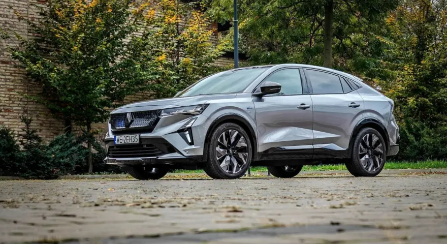 Nowy Renault Rafale, elegancki SUV coupe, prezentuje się na tle jesiennej zieleni i ceglanej ściany.
