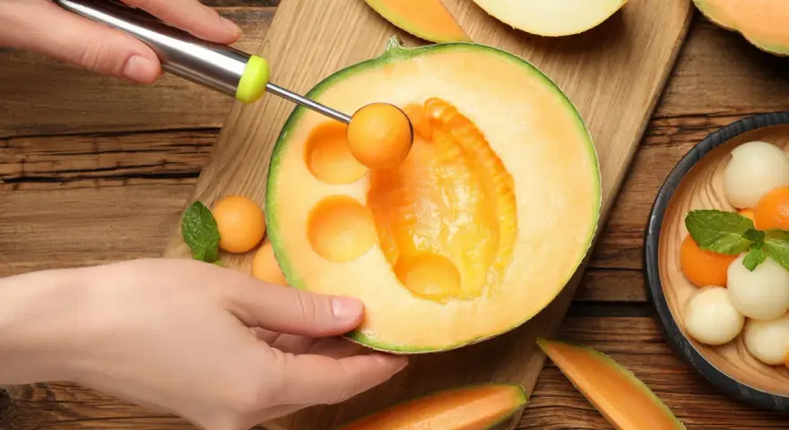 Ręka z gałkownicą wydobywa kulki z melona, ukazując jego soczyste wnętrze. Melon właściwości odżywcze czynią go idealnym na letnie orzeźwienie.