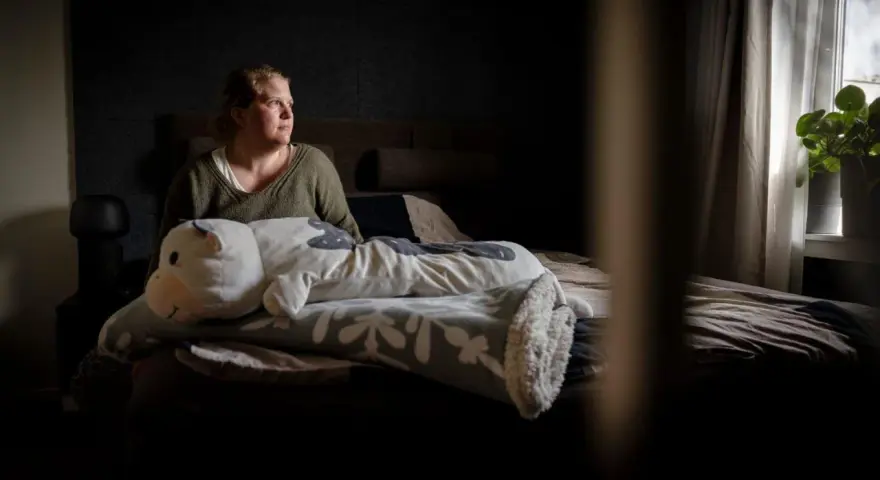 En kvinna sitter i sängen med en stor kramdjursko. Hon ser ut att fundera, kanske över sina två personligheter.