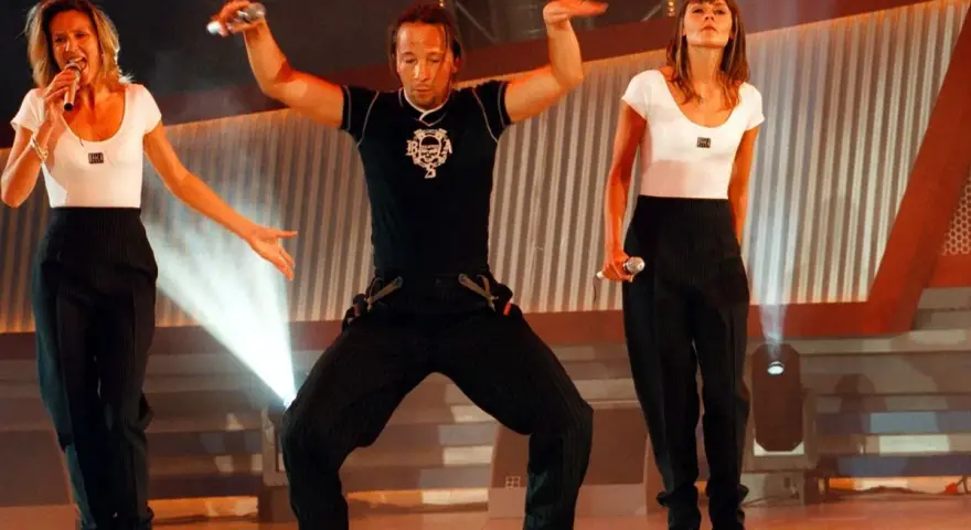 Drei Künstler in Schwarz-Weiß-Outfits performen auf einer Bühne. Die Frau links singt, der Mann in der Mitte tanzt, die Frau rechts hält ein Mikrofon. Ein energiegeladener Moment für **dance & electronic** Musik.