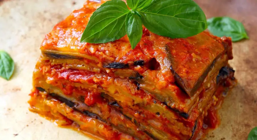 Una fetta di parmigiana di melanzane, stratificata e succulenta, guarnita con basilico fresco.