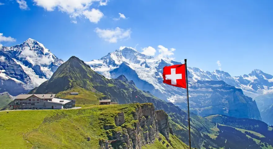 A Swiss flag flies proudly against a backdrop of majestic snow-capped mountains and lush green slopes, showcasing the beautiful places of nature in Switzerland.