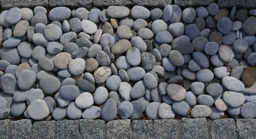 Gładkie, szare kamienie tworzą naturalną dekorację w ogrodzie, otoczone granitową kostką.