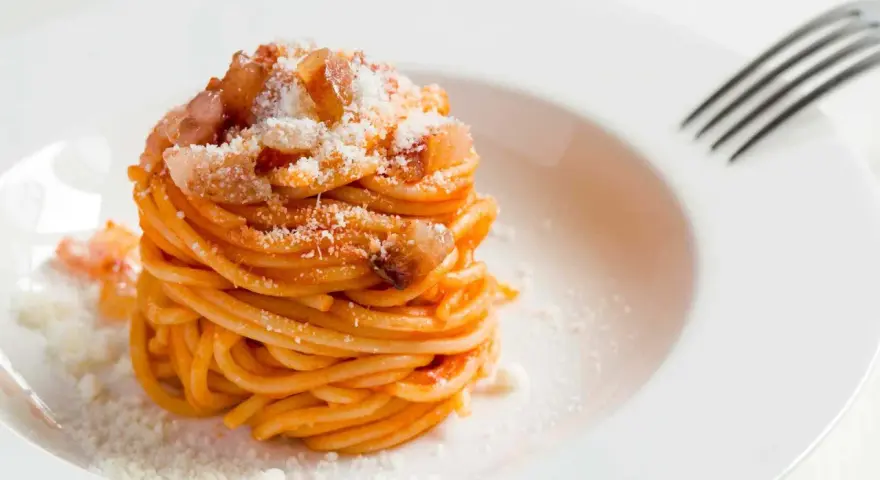 Un piatto di spaghetti alla amatriciana ricetta, conditi con guanciale croccante e pecorino grattugiato, pronti per essere gustati.
