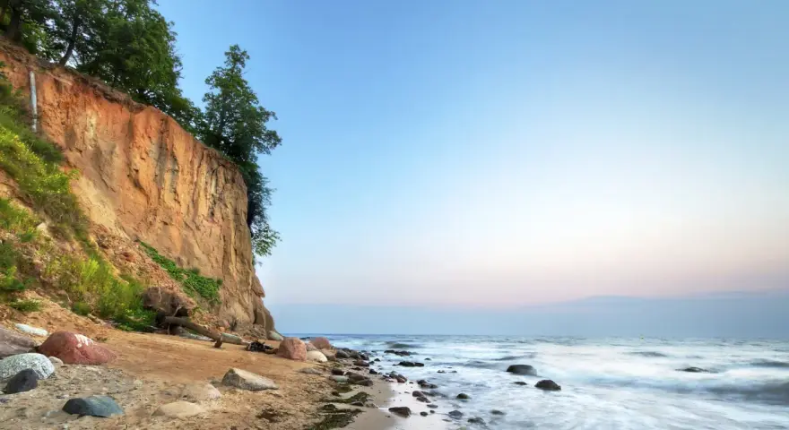 Piękna linia brzegowa Bałtyku w Polsce z klifem porośniętym drzewami i piaszczystą plażą.