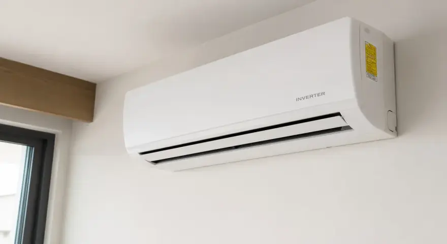 Unidad de aire acondicionado blanca con tecnología inverter, montada en pared blanca, cerca de una ventana.