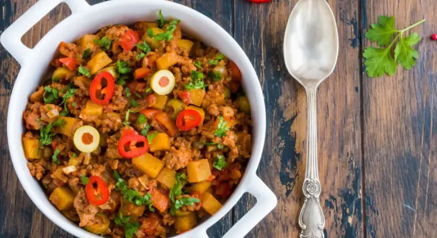 Pyszne danie z mielonego mięsa wołowego z ziemniakami, oliwkami i papryczką chili, posypane natką pietruszki.