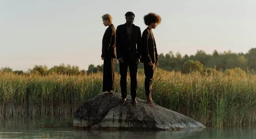 Trois personnes en noir, sur un rocher au milieu de l'eau, symbolisant la non monogamie éthique et la liberté de choix.