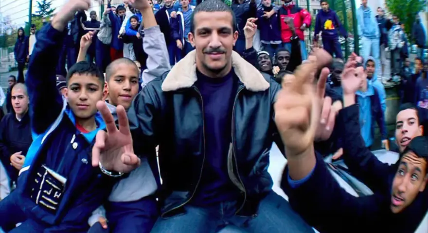Un chanteur rap français, entouré de jeunes fans, pose avec confiance.