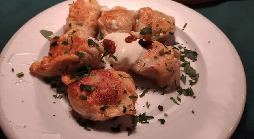 Pierogi, un piatto tipico polacco, serviti su un piatto bianco con panna acida e prezzemolo tritato.
