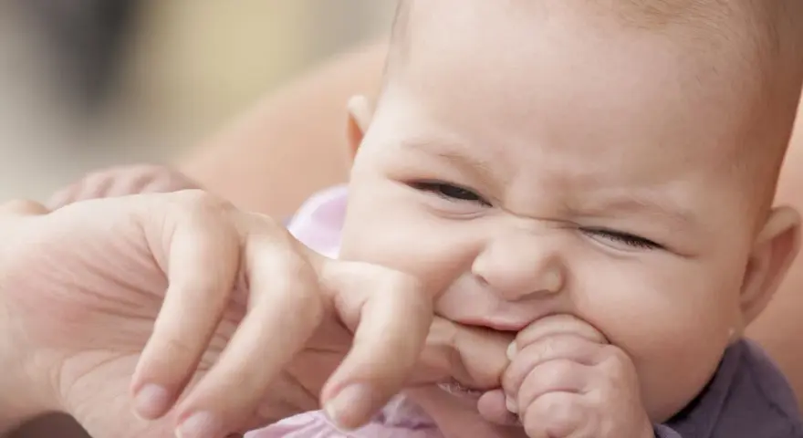 Ein süßes Baby mit einem lustigen Gesichtsausdruck, das gerade versucht, den Finger einer erwachsenen Person zu beißen.