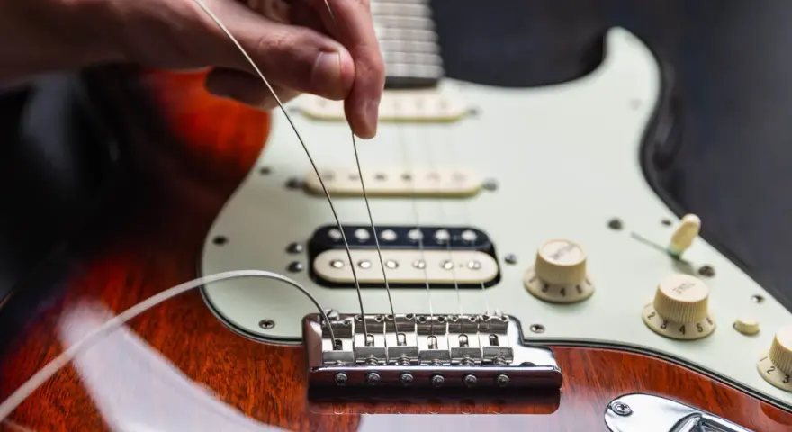 Dłoń naciąga nowe struny w gitarze elektrycznej, przygotowując ją do gry.