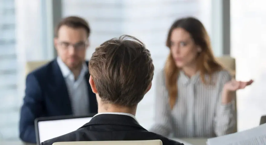 Besprechung mit einem Anwalt über Versicherungsansprüche. Eine Frau gestikuliert, während ein Mann mit Brille und ein Mann im Vordergrund zuhören.