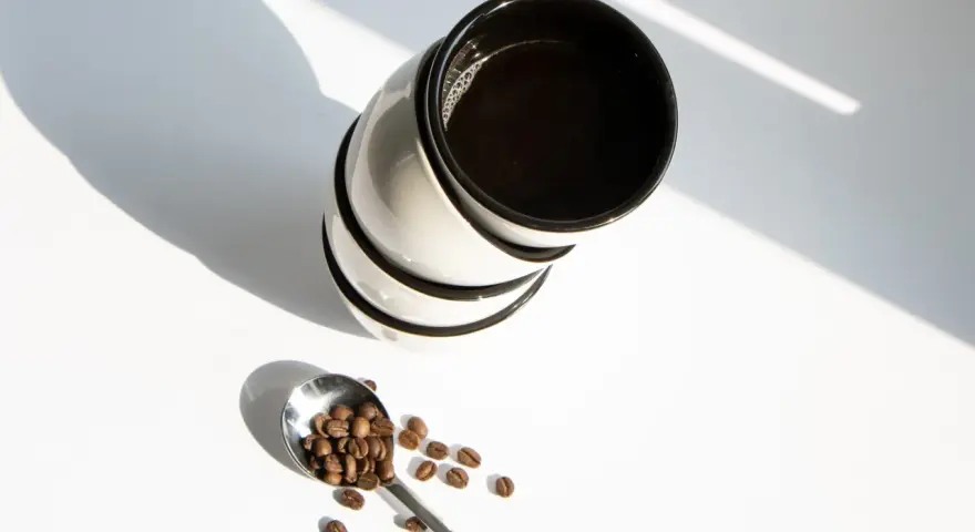 Stos kawy w filiżankach i łyżka z ziarnami kawy. Zastanawiasz się, ile kofeiny ma kawa w 100 ml?
