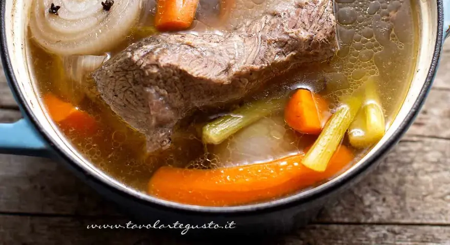 Un pezzo di carne succulenta cuoce lentamente in un brodo di carne ricco, con carote, sedano e cipolla.