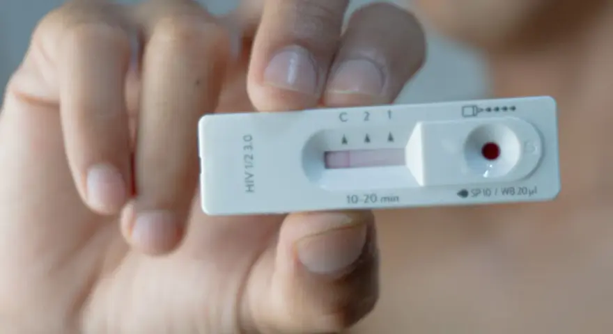 Dłoń trzyma test na HIV z widocznym wynikiem.