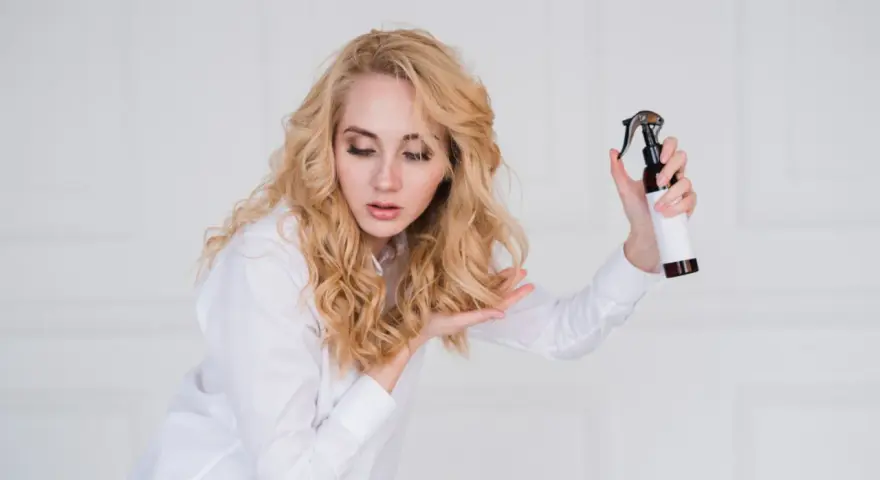 Blondynka z pięknymi, naturalnymi falami na włosach testuje nowy spray do stylizacji.