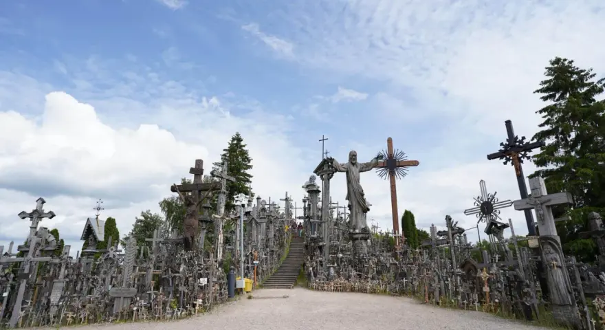 A vast mountain of crosses, with a statue of Jesus at its peak, stands under a cloudy sky.