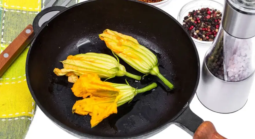 Fiori di zucca in padella, pronti per essere impanati e fritti. Accanto, spezie e sale per insaporire.