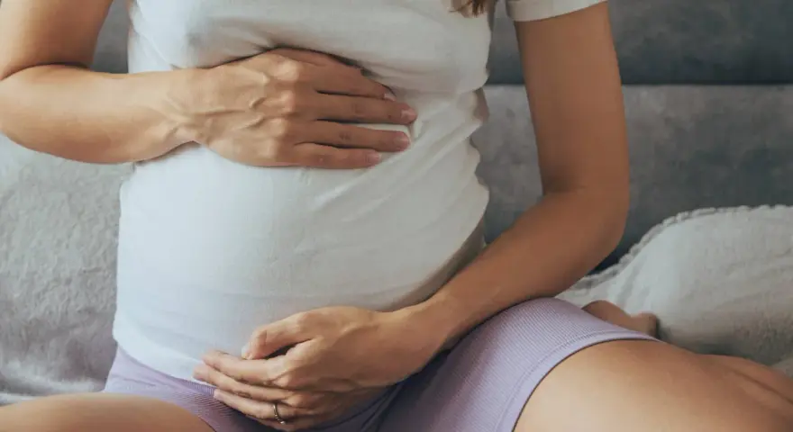 Brzuch kobiety w ciąży, z dłońmi delikatnie go obejmującymi.