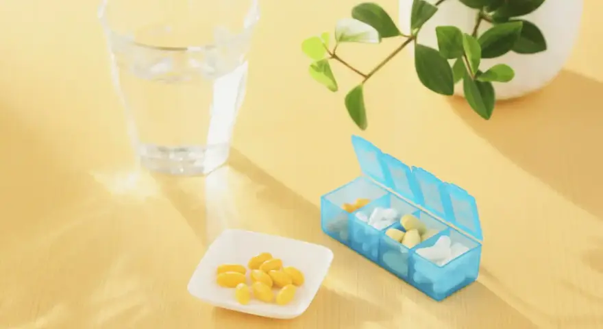 Un bicchiere d'acqua, una ciotolina con capsule gialle e un portapillole blu. Forse integratori per capire cosa sono gli elettroliti.
