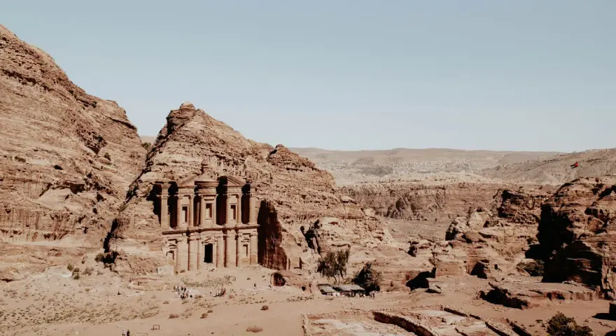 The ancient jordan ruins of Petra, carved into sandstone cliffs, stand majestically under a clear blue sky.
