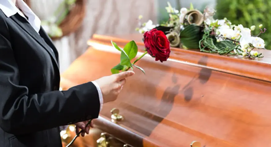 Eine Frau in Trauer legt eine rote Rose auf den Sarg. Sie muss die Beerdigung ihres getrennt lebenden Ehemanns bezahlen.