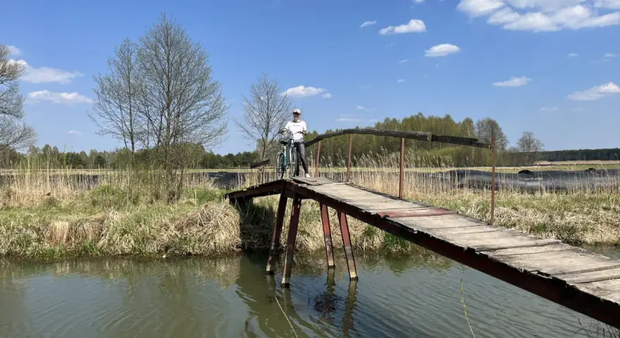 Osoba z rowerem na drewnianym mostku nad rzeką. Piękny dzień na odkrywanie tras rowerowych łódzkiego.