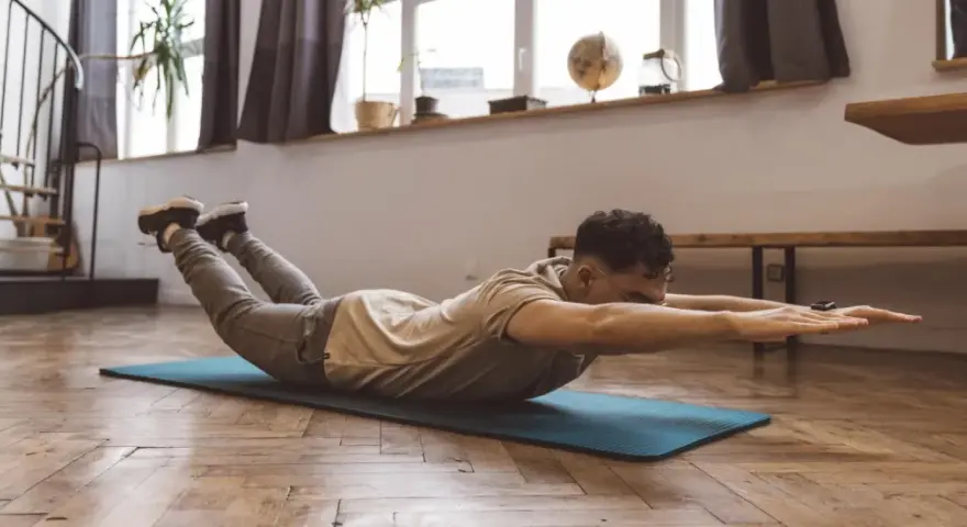 Homme faisant un exercice dos sur un tapis, bras tendus, jambes levées.