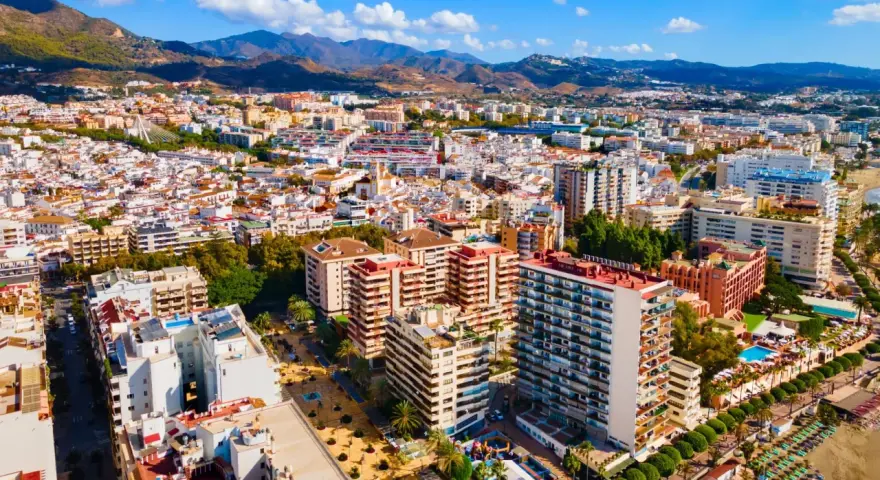Widok z lotu ptaka na nadmorskie miasto Marbella, z górami w tle. Widać plażę, hotele i budynki mieszkalne.