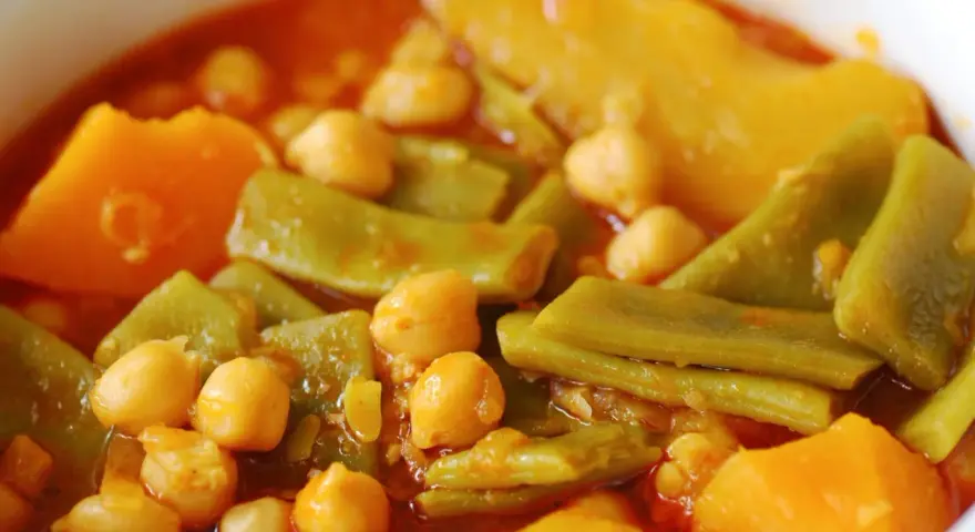 Un plato humeante de olla gitana, con garbanzos tiernos, judías verdes y trozos de calabaza en un rico caldo.