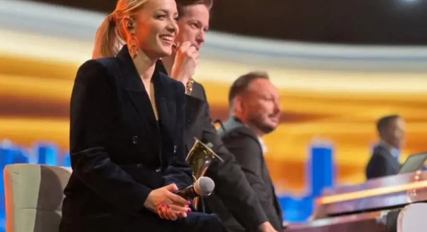Uśmiechnięta wokalistka, która śpiewa w "Jaka to melodia", siedzi obok pianistów na scenie.