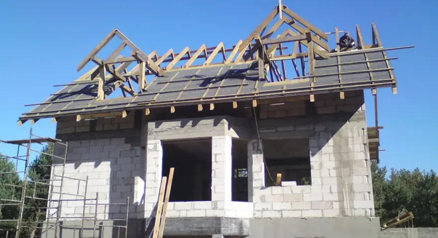 Na dachu budowy domu z betonu komórkowego widać drewnianą konstrukcję i wiechę.