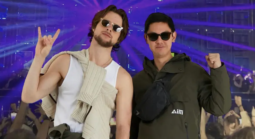 Deux amis profitent d'un concert, l'un fait un signe rock'n'roll, l'autre un poing levé. Leur tenue festival pluie est parfaite pour l'ambiance.