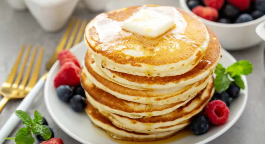 Pile de pancakes sans oeuf, dorés et moelleux, garnis de beurre fondant et de fruits rouges frais. Un délice pour le petit-déjeuner !
