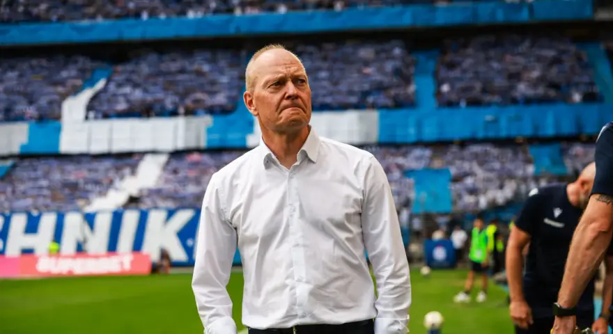 Trener w białej koszuli na tle trybun pełnych kibiców podczas meczu Widzew Łódź – Lech Poznań.