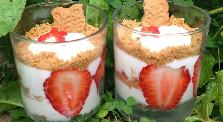 Deux verrines de tiramisu fraises spéculoos, garnies de crème, fraises fraîches et biscuits spéculoos, posées sur un lit de verdure.