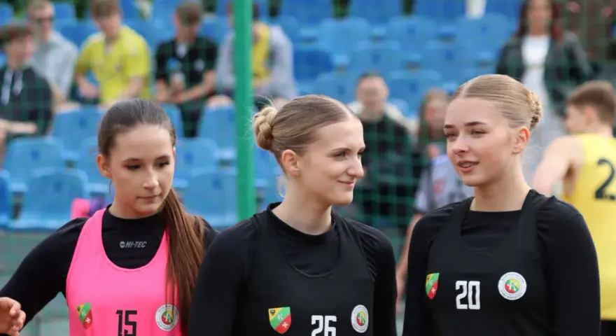 Trzy młode zawodniczki KPR Kobierzyce w sportowych strojach, z numerami 15, 26 i 20, na tle trybun.