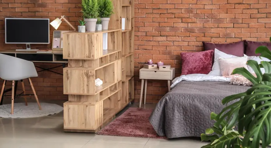 Soluzione d'arredo per un monolocale di 40 mq: libreria divisoria, scrivania, letto accogliente e piante verdi creano uno spazio funzionale e di stile.