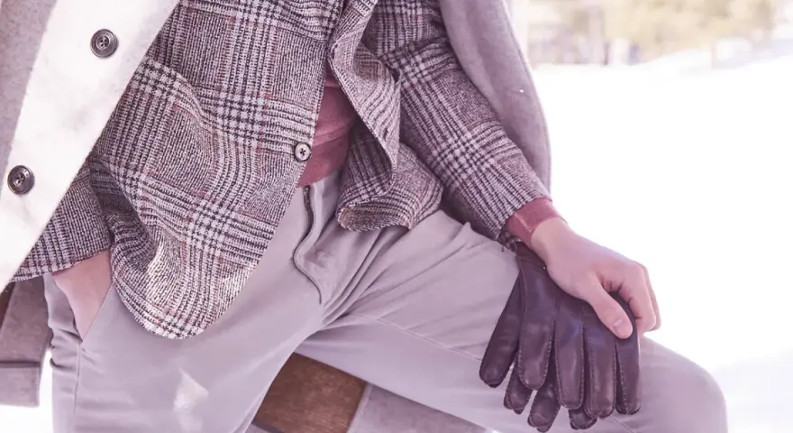 Un uomo indossa un elegante spezzato con giacca a quadri, maglione rosa e guanti in pelle marrone, pronto per l'inverno.
